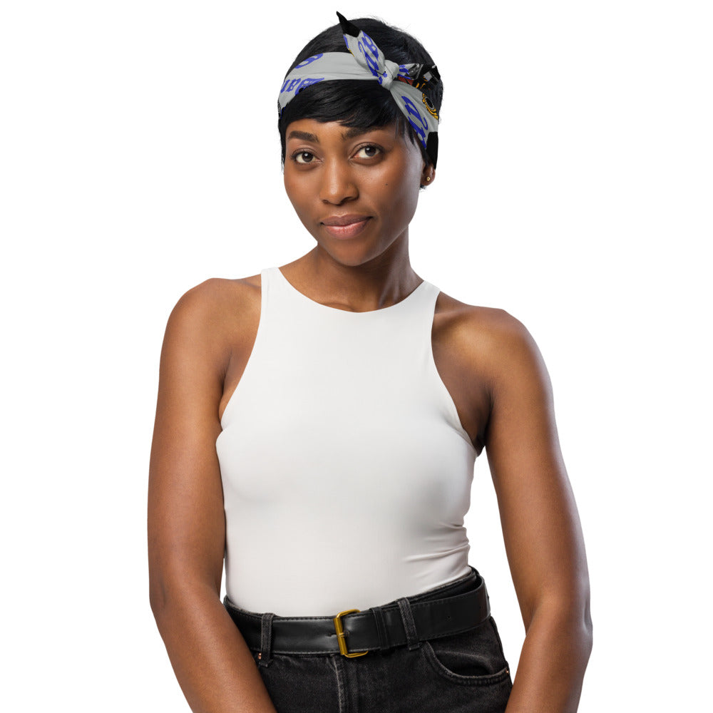 Woman wearing a grey printed headscarf, white tank top, and black belted jeans