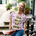 Woman in pink graphic t-shirt with black spiders and bold yellow script outdoors by bike