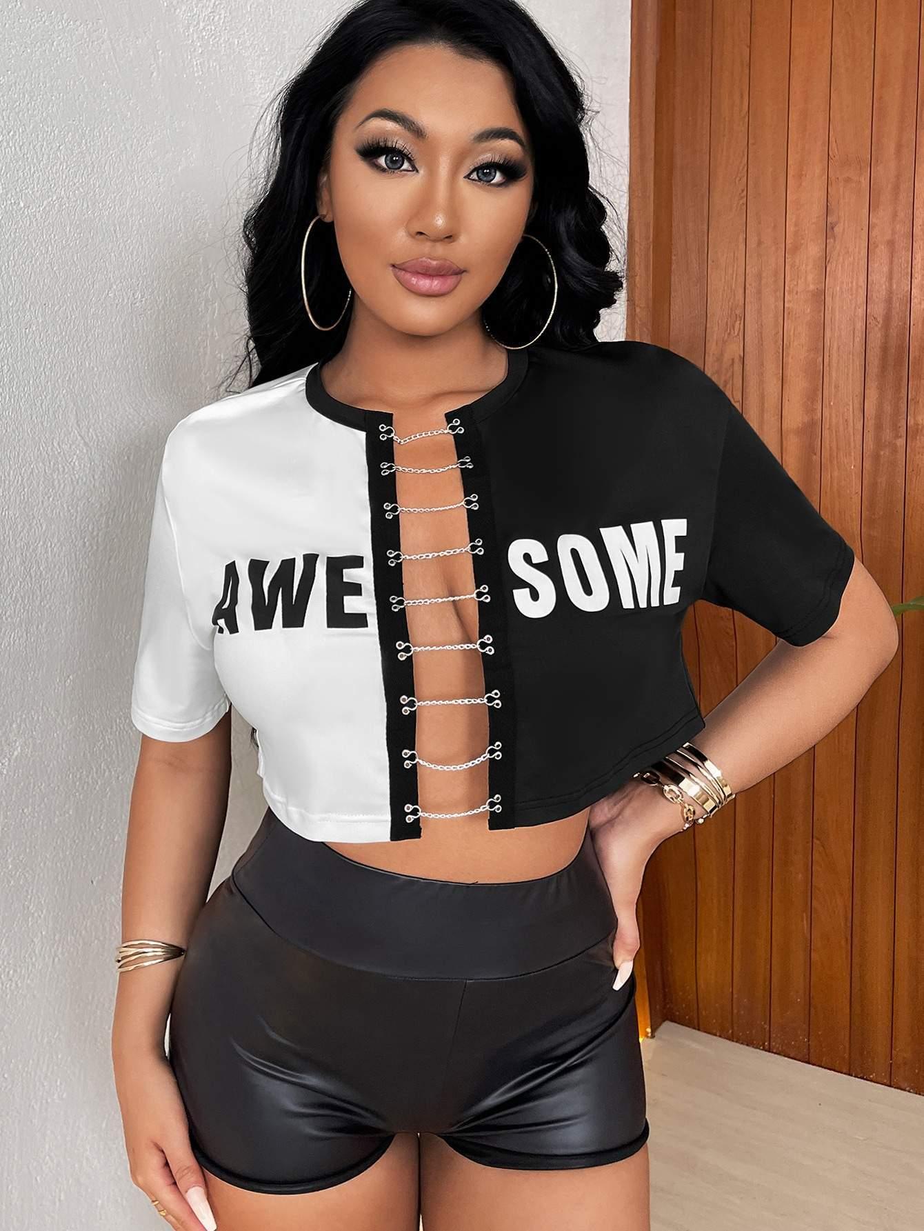 Woman wearing a black and white split crop top with chain detail and 'AWESOME' text, paired with high-waisted black shorts.